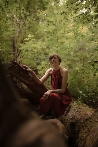A woman in a red dress sitting on a log in the woods, seeking Reiki Healing or Shamanic Healing.