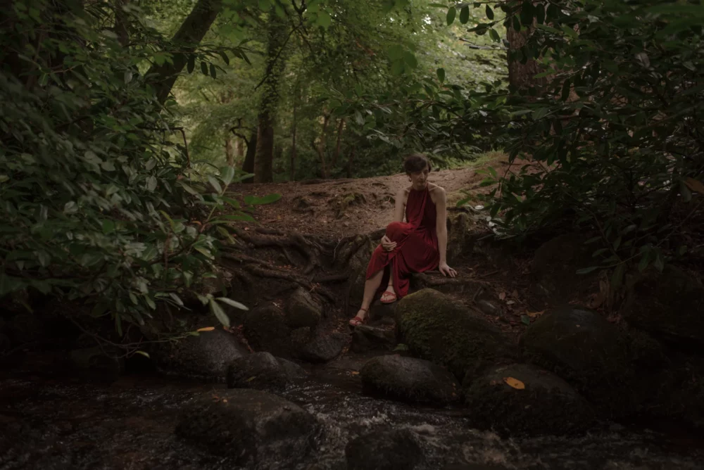 A woman in a red dress sitting on rocks in a forest experiences the soothing essence of Reiki Healing.