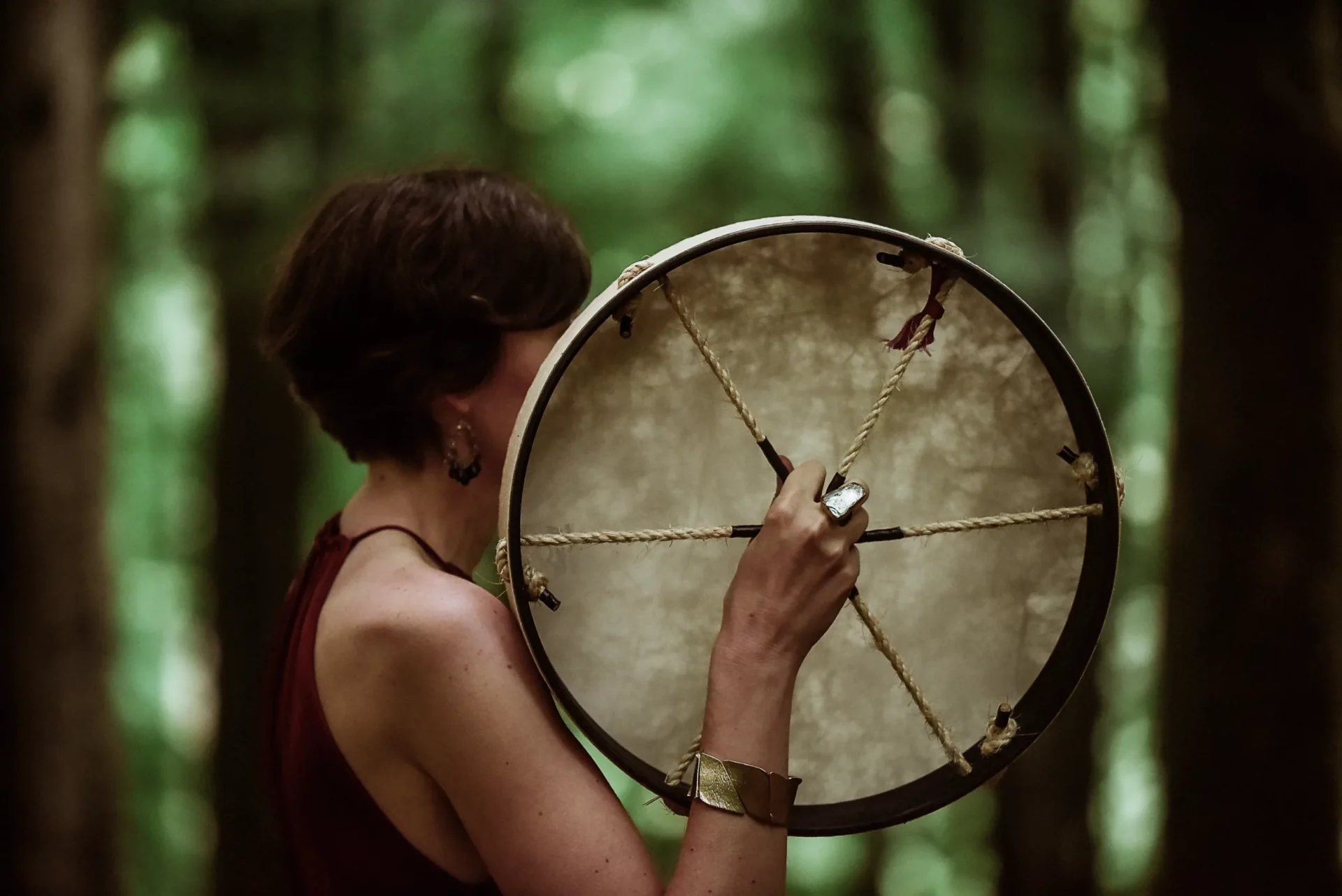 A shamanic healer gracefully holds a large drum amidst the serene woods of Ireland.